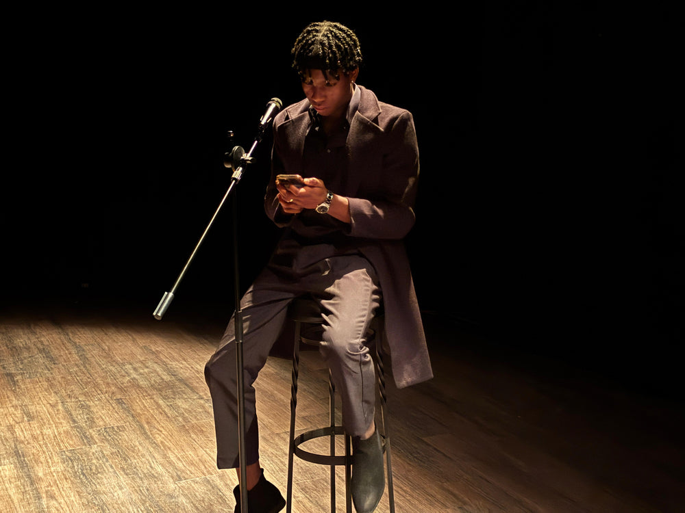 Allein auf der Bühne mit Mikrofon – ein junger Mann sammelt sich für den nächsten Schritt. Self-Improvement beginnt mit dem Mut, sichtbar zu werden.